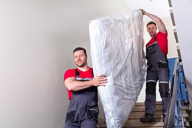 two workers carrying a heavy box spring out of a bedroom in Centerton